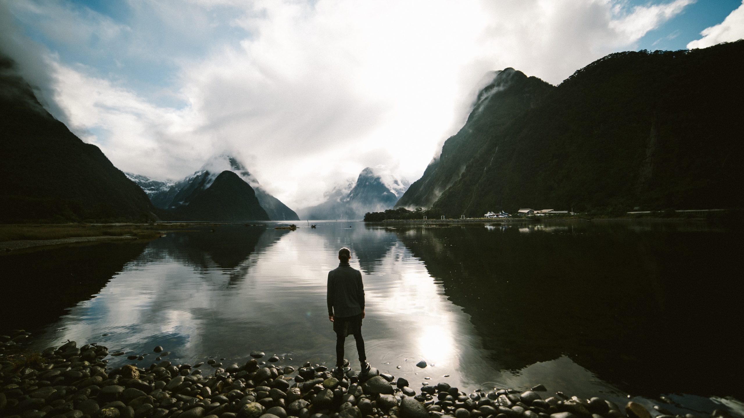 Eine Berglandschaft, davor ein See mit einem meditierenden Menschen auf einem Steg